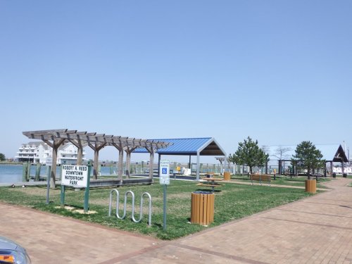 A park with wooden structures, grassy areas, and a sign reading "Poetry in the Park" under a hazy sky.