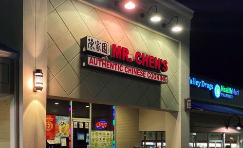 Sign for Mr. Chen's Authentic Chinese Cooking illuminated at night, with nearby shops visible in the background.
