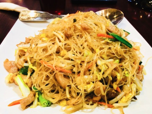 A plate of stir-fried noodles with vegetables and chicken, garnished and served on a white dish.