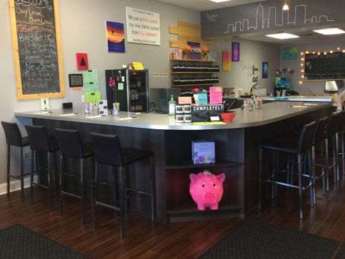 A cozy café interior featuring a curved counter, colorful artwork, and a pink pig decoration on a shelf.