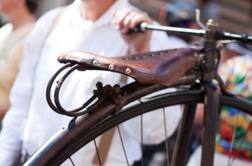 A close-up of a vintage bicycle seat held by a person in a white shirt, with a blurred crowd in the background.