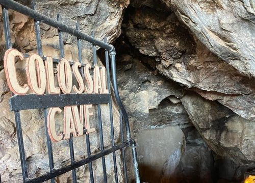 Entrance gate to Colossal Cave, surrounded by rocky walls and dimly lit pathways leading into the cave.