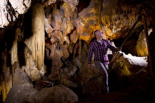 A person explores a dimly lit cave, surrounded by rock formations and stalactites, while climbing a staircase.