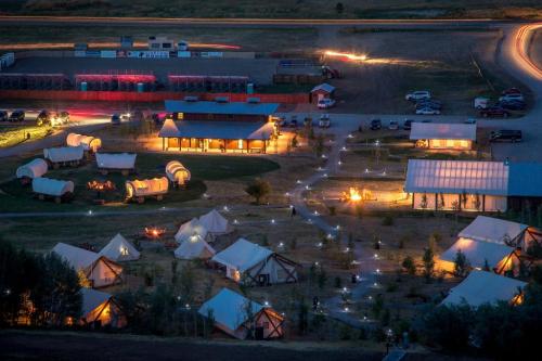 Aerial view of a campsite at night, featuring tents, wagons, and illuminated pathways, with vehicles in the background.