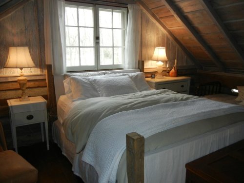 Cozy attic bedroom with a double bed, wooden beams, two lamps, and a window letting in natural light.