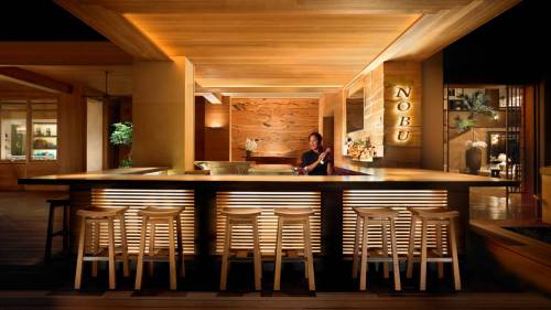 A sleek wooden bar at Nobu restaurant, featuring a bartender and stylish stools in a warm, modern setting.