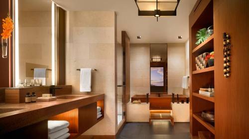 Modern bathroom with wooden accents, a large mirror, and a soaking tub, featuring elegant decor and soft lighting.