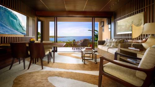 A stylish living room with ocean views, featuring modern furniture, a large wave painting, and warm wood accents.