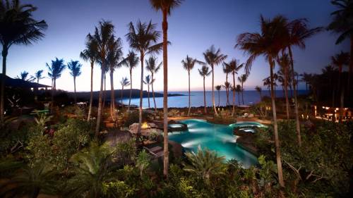 Tropical resort at dusk with a pool, palm trees, and ocean view under a colorful sky.