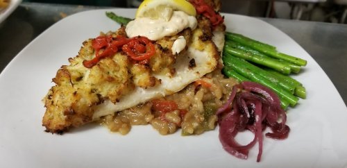A plate featuring baked fish topped with crab, served with asparagus, risotto, and pickled onions.