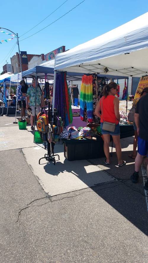 A vibrant outdoor market with colorful tents displaying clothing and accessories, and people browsing the stalls.