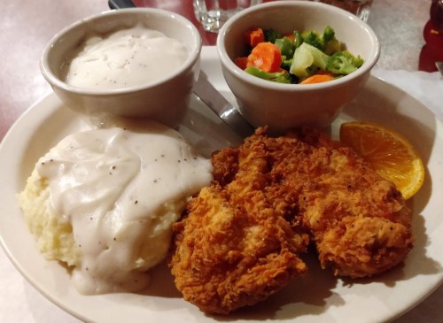 A plate with fried chicken, mashed potatoes with gravy, a side of mixed vegetables, and an orange slice.