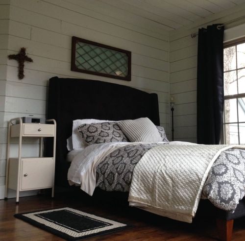 Cozy bedroom featuring a dark bed frame, patterned bedding, a nightstand, and a window with natural light.