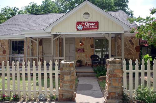 A charming stone house with a white picket fence, featuring a sign that reads "The Crazy Bake House."