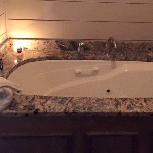 A cozy bathroom scene featuring a white bathtub with a granite countertop and a lit candle nearby.