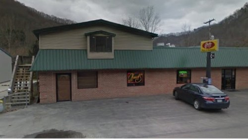 A brick building with a green metal roof, featuring a sign that says "Open" and a parked car in front.