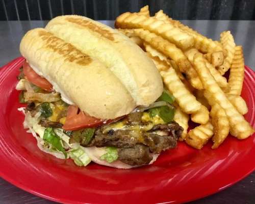 A toasted sandwich filled with meat, lettuce, tomatoes, and cheese, served with a side of crispy crinkle-cut fries.