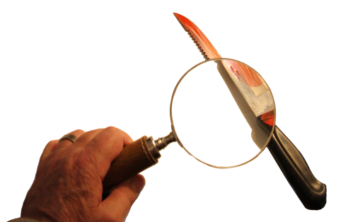 A hand holding a magnifying glass, focusing on a knife with a serrated edge against a black background.