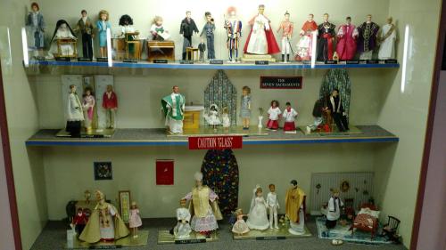 A display of figurines representing various religious sacraments and ceremonies, arranged on shelves.