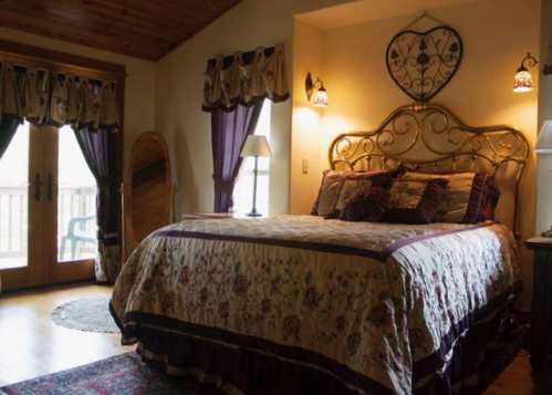 Cozy bedroom with a floral bedspread, decorative lamps, and a balcony door, featuring warm wooden accents.