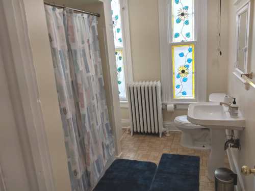 A bright bathroom featuring a shower curtain, sink, toilet, and colorful stained glass windows.