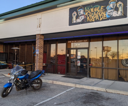 A blue motorcycle parked outside the Double Dragon Arcade, featuring a colorful sign above the entrance.