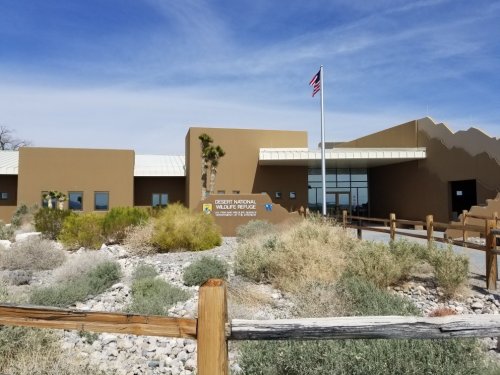 Desert National Wildlife Refuge visitor center with a flag, surrounded by desert vegetation and mountains in the background.