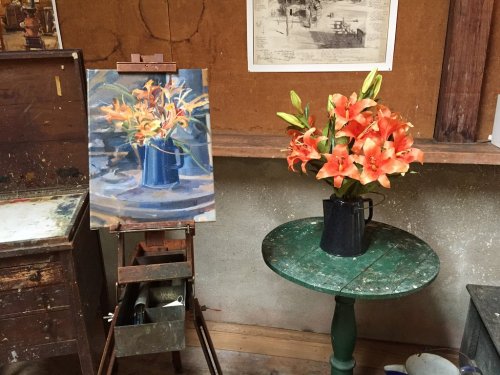 A still life scene featuring a vase of orange lilies on a green table, alongside a painted version on an easel.