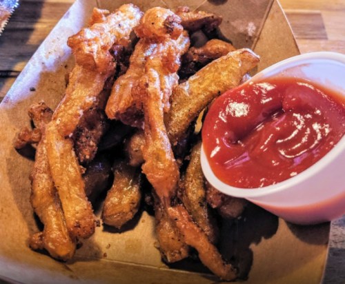 Crispy fried potato strips served with a side of ketchup in a small container.