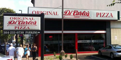 Exterior of Di Carlo's Pizza, featuring a sign and storefront with people walking by.