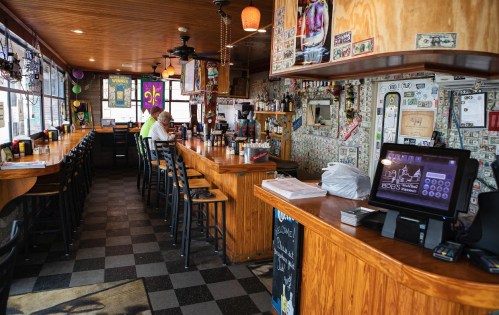 A cozy bar interior with wooden counters, a cash register, and walls decorated with dollar bills and colorful art.