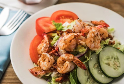 A plate of shrimp salad featuring grilled shrimp, lettuce, tomatoes, and cucumber slices.