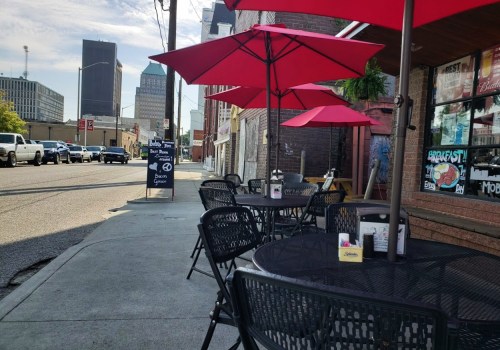Outdoor café scene with black tables and red umbrellas along a city street, featuring a sign for breakfast.