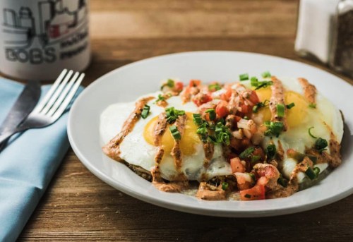 A plate of eggs topped with diced tomatoes and green onions, drizzled with sauce, on a wooden table.
