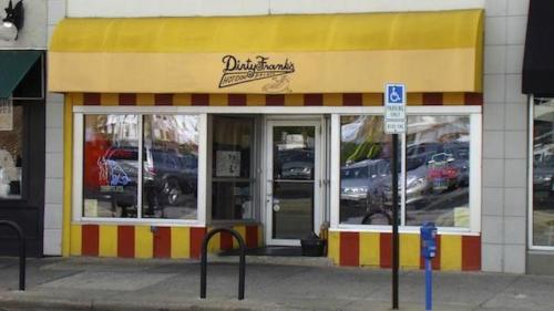 A storefront with a yellow awning and red-striped facade, featuring large windows and a parking meter outside.