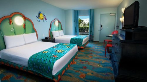 Brightly colored hotel room with two beds, ocean-themed decor, and a view of the outdoors through a large window.