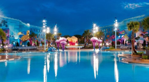 A vibrant pool area at night, featuring colorful decorations, palm trees, and illuminated jellyfish sculptures.