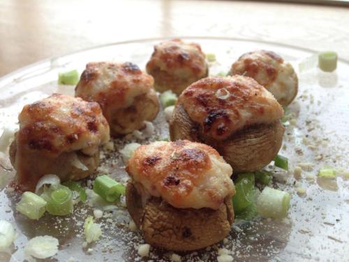 A plate of stuffed mushrooms topped with melted cheese and garnished with chopped green onions.