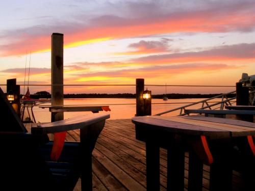 A serene sunset over water, viewed from a wooden dock with chairs and lanterns, creating a peaceful atmosphere.