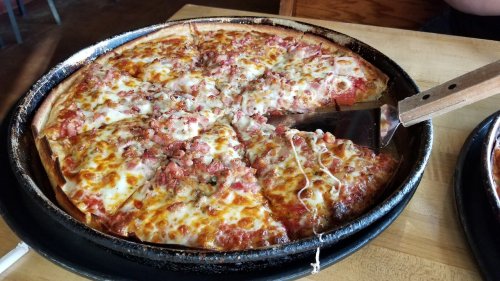 A freshly baked pizza with melted cheese and toppings, partially sliced and served on a wooden table.