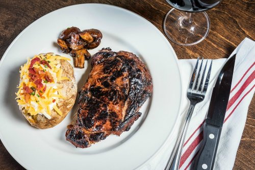 A plate with a grilled steak, a loaded baked potato, sautéed mushrooms, and a glass of red wine.