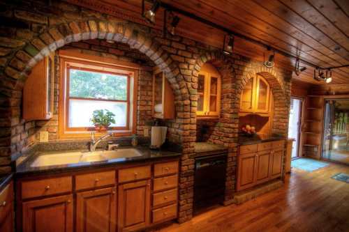 Cozy kitchen with brick arches, wooden cabinets, and a sink under a window, featuring warm wood accents and natural light.