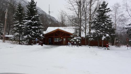 A log cabin-style building surrounded by snow-covered trees, with a snowy path leading to the entrance.