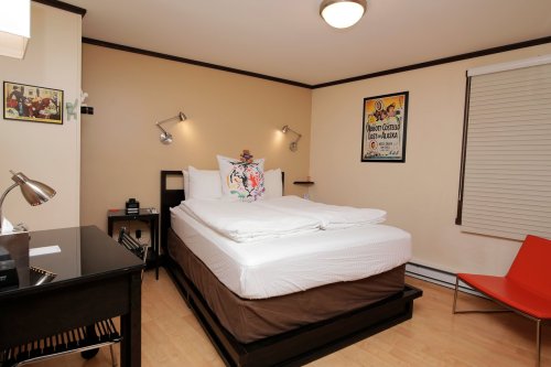 Cozy hotel room with a bed, desk, and orange chair, featuring warm lighting and decorative wall art.