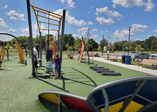 A vibrant playground with climbing structures and children playing on green turf under a sunny blue sky.