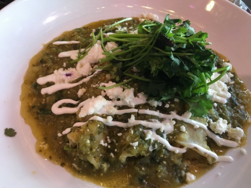 A plate of green enchiladas topped with cilantro, cheese, and drizzled with sour cream.