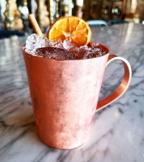 A copper mug filled with ice and a drink, garnished with a dried orange slice and a cinnamon stick.