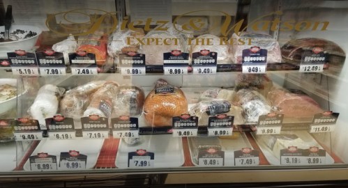A refrigerated display case filled with various meats, each labeled with prices and brand information.
