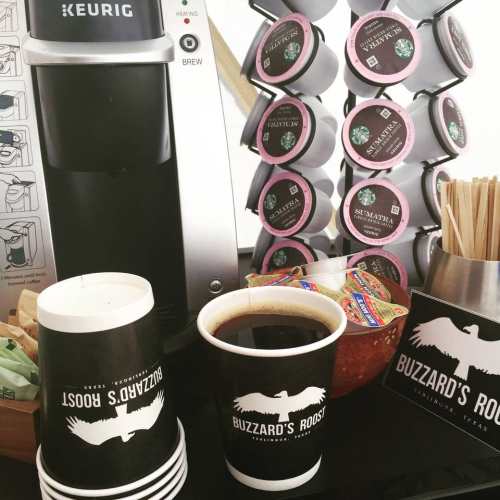 A coffee station featuring a Keurig machine, coffee pods, cups, and condiments at Buzzard's Roost.