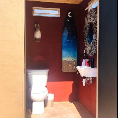 A rustic bathroom featuring a toilet, sink, and decorative elements like a mirror and wall art.